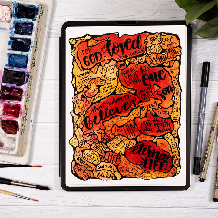 iPad with artistic text design on a white surface with art supplies