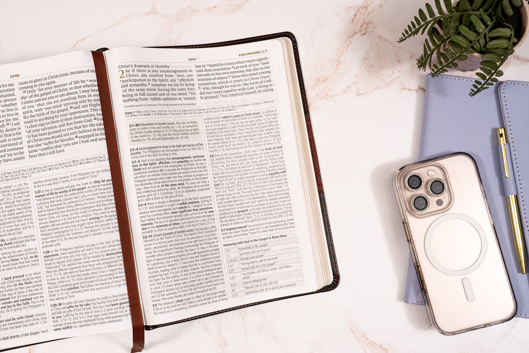Open bible with a phone and pen on a light surface
